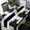 A long dining table set featuring black and white placemats, napkins, and cutlery on a white tablecloth.