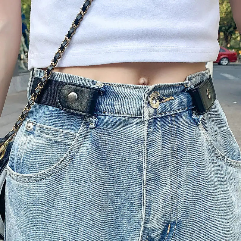 A close-up of a person wearing a white crop top and light wash denim jeans with a black leather belt.