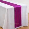 Elegant satin table runner in purple and white on a draped white tablecloth.