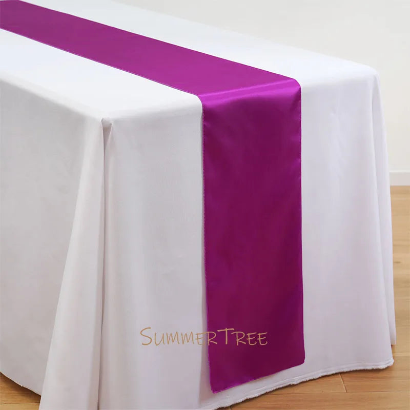 Elegant satin table runner in purple and white on a draped white tablecloth.