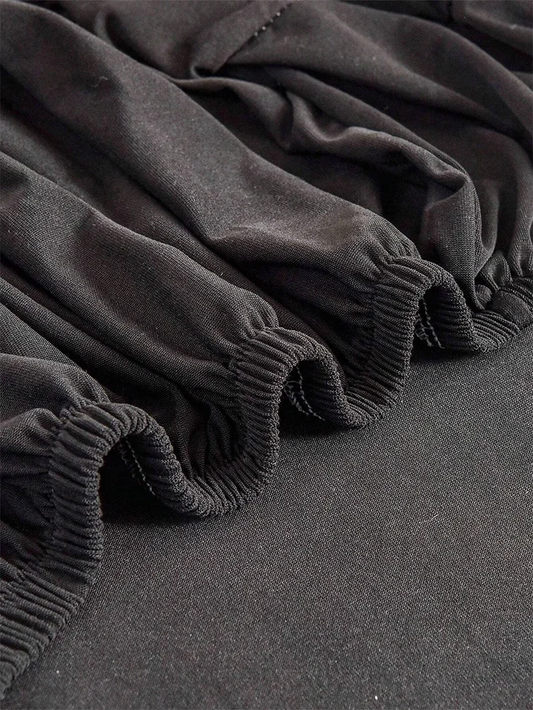Black elastic sofa slipcovers draped and folded on a dark gray fabric.