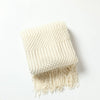 A cream-colored oversized knitted tassel throw blanket folded on a white surface.