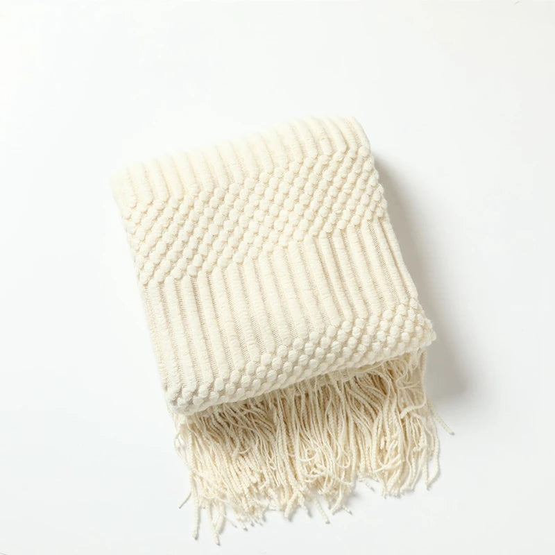 A cream-colored oversized knitted tassel throw blanket folded on a white surface.