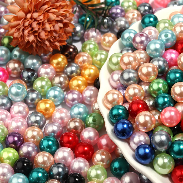 A close-up of various colored imitation pearl beads in shades of pink, green, blue, and gold scattered on a white surface.