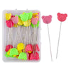 A clear plastic box containing dressmaking pins with colorful pink and green heads and metal pins.