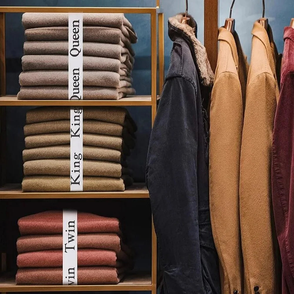 A display of stacked bed sheets labeled Queen, King, and Twin in various earth tones on wooden shelves.