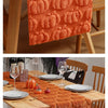 An orange textured table runner with pumpkin designs is laid on a wooden dining table set for a festive meal.