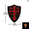A black shield-shaped embroidered patch featuring a red cross with the text DEUS VULT in gold thread.