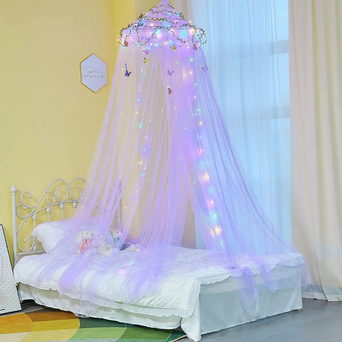 A purple decorative mosquito net bed curtain with sparkling lights draped over a white bed.