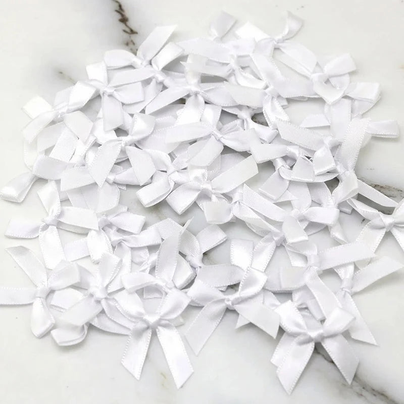 A pile of small white satin ribbon bows for crafts and decor scattered on a white marble surface.
