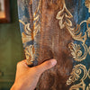 A hand touches a close-up of brown sheer curtains with gold floral embroidery.