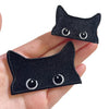 A pair of embroidered black cat iron-on patches with white eyes are shown being held in a hand.