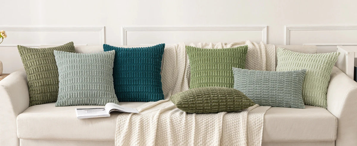 A collection of textured, striped throw pillows in various shades of green and teal displayed on a light-colored sofa.