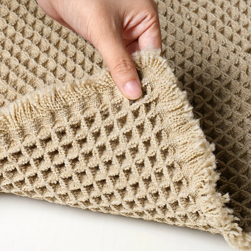 A hand is touching a beige waffle texture bath mat for floors.