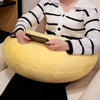 A person wearing a striped sweater is holding a smartphone while resting on a large yellow throw pillow.