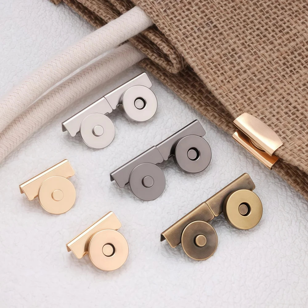 A collection of seamless magnetic button clasps in gold and silver tones resting on a beige fabric.