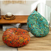 A vibrant teal and green bohemian cotton linen throw cushion resting on a wooden table next to an orange patterned cushion.