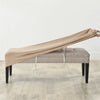 A beige velvet bench slipcover draped over a light gray upholstered bench with visible securing straps.