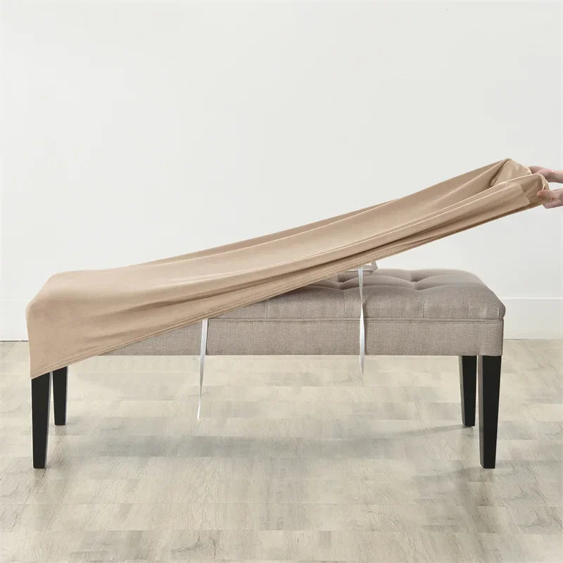 A beige velvet bench slipcover draped over a light gray upholstered bench with visible securing straps.