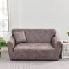 A modern taupe PU leather sofa slipcover in a living room setting with a light gray wall and wooden floor.