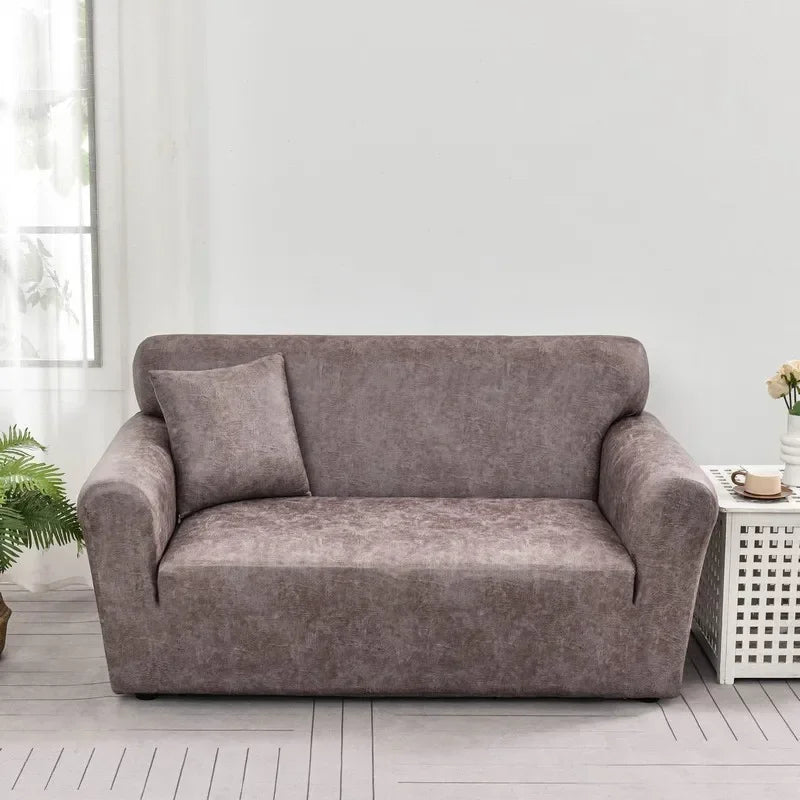 A modern taupe PU leather sofa slipcover in a living room setting with a light gray wall and wooden floor.