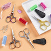 A collection of vintage stainless steel sewing scissors, various colored threads, and a black leather tool on a white tray.