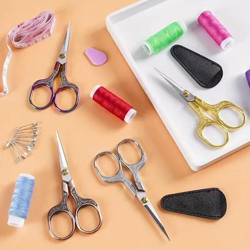 A collection of vintage stainless steel sewing scissors, various colored threads, and a black leather tool on a white tray.