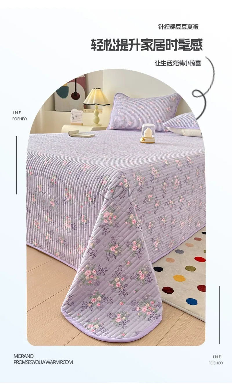 A lilac floral quilted bedspread draped over a bed, emphasizing soft texture and light.