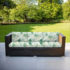 Woven rattan outdoor sofa cushion cover in light green floral pattern placed on a patio.