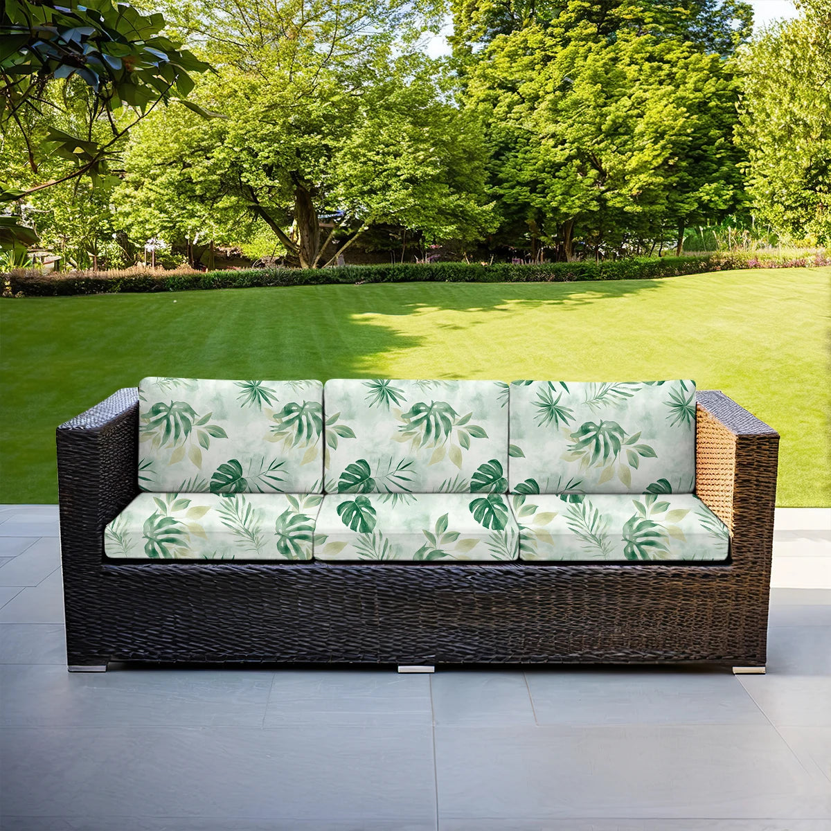 Woven rattan outdoor sofa cushion cover in light green floral pattern placed on a patio.