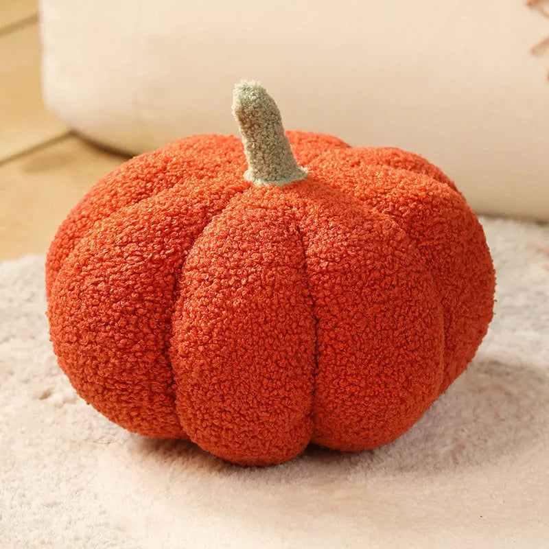 An orange plush pumpkin throw pillow with a green stem resting on a light surface.