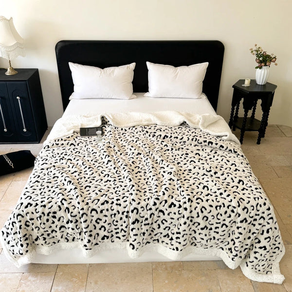 A white leopard print knit throw blanket is draped over a bed with white pillows.