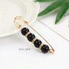Gold-toned adjustable pearl brooch featuring black beads and gold accents on a thin wire.