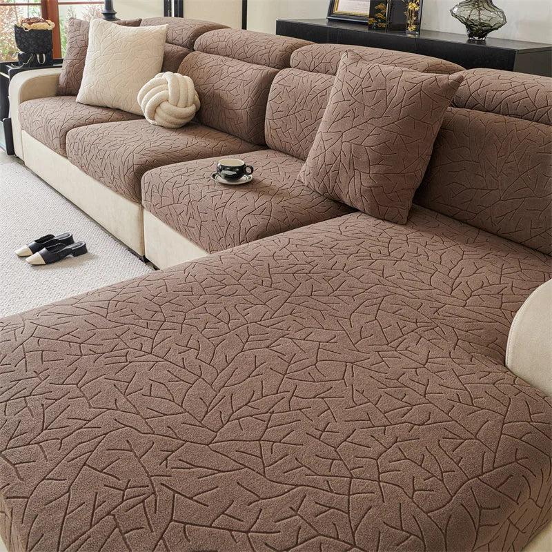 A brown jacquard sofa cover featuring a branch pattern and cream accent pillows on a beige sofa.
