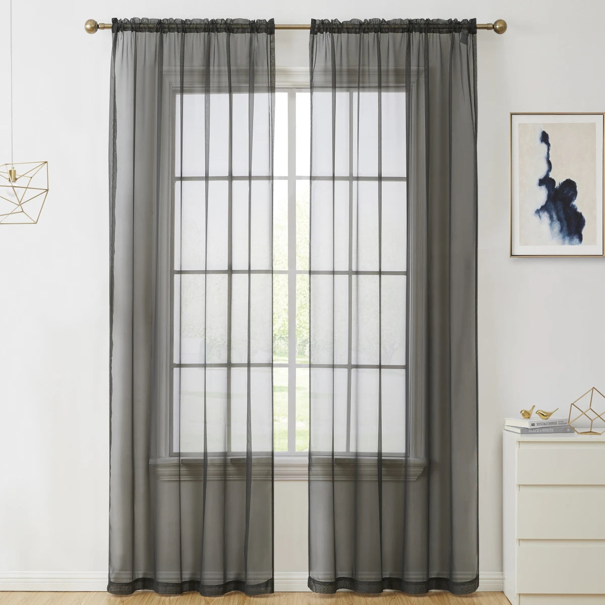 A pair of charcoal gray sheer voile curtains hanging on a window with a white frame.
