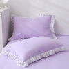 A purple ruffled pillowcase with a white trim is displayed on a bed.