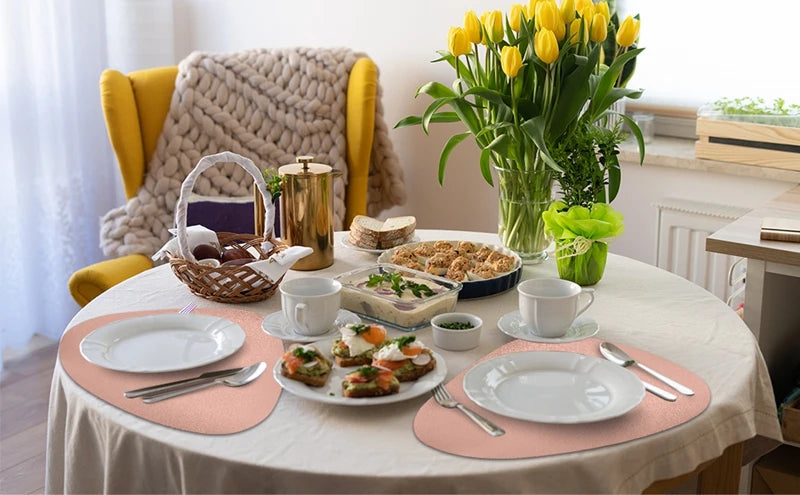 A white table set with pink placemats, plates, silverware, and food, surrounded by yellow and beige textiles.