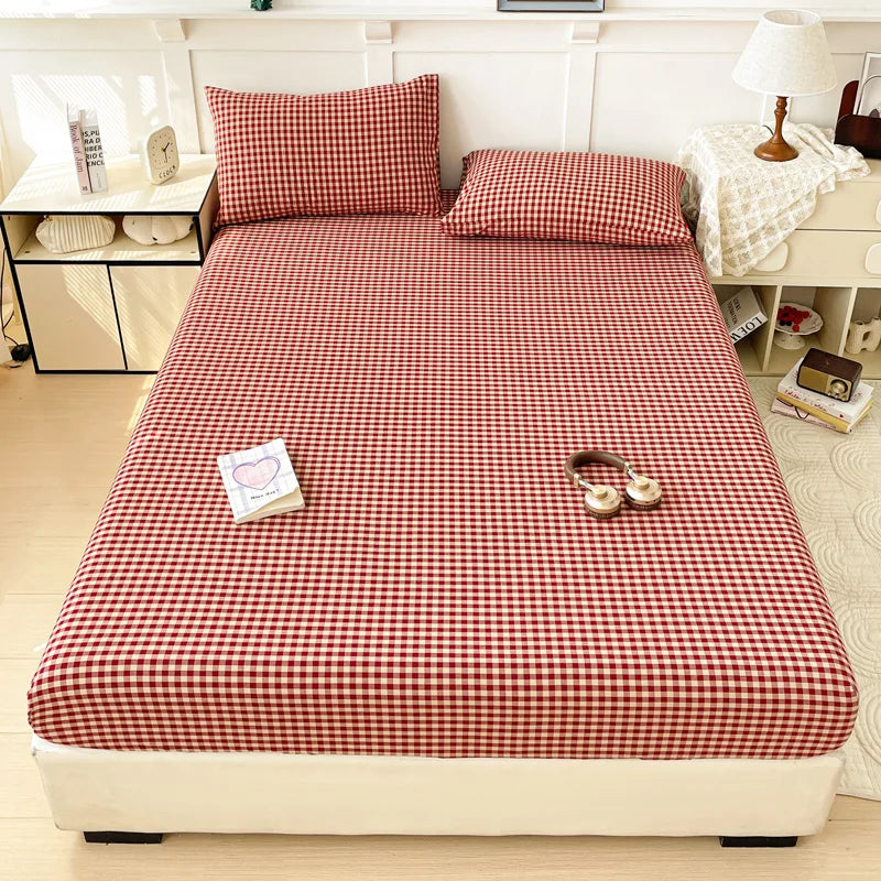 A red and white checkered fitted sheet displayed on a bed with matching pillows and surrounding furniture.