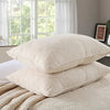 A set of cream embroidered cotton quilted pillows resting on a beige quilted bedspread near a window.