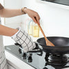 A person is using a wooden utensil to stir food in a black pan on a stovetop.