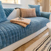 A teal quilted velvet sofa protection cover with a beige throw pillow and matching blanket on a light-colored sofa.