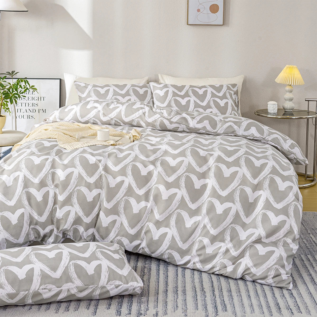 A light gray duvet cover set featuring a white heart print on a bed with natural light and a yellow lamp.