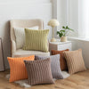 A collection of beige and olive faux fur stripe decorative throw pillows displayed on a wooden floor.