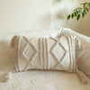A cream knit pillow cover with geometric stitching rests on a light-colored sofa.