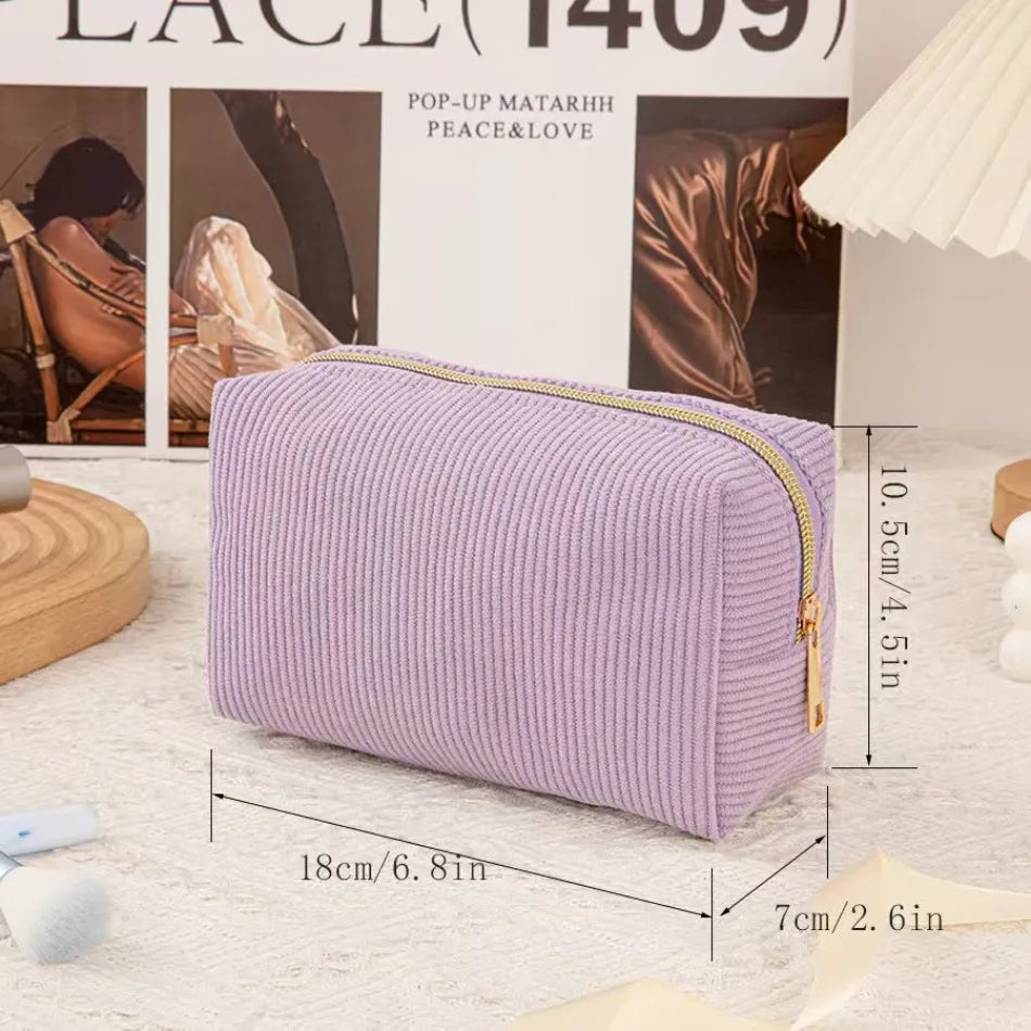 A lavender ribbed cosmetic storage pouch with a gold zipper displayed on a white textured surface.