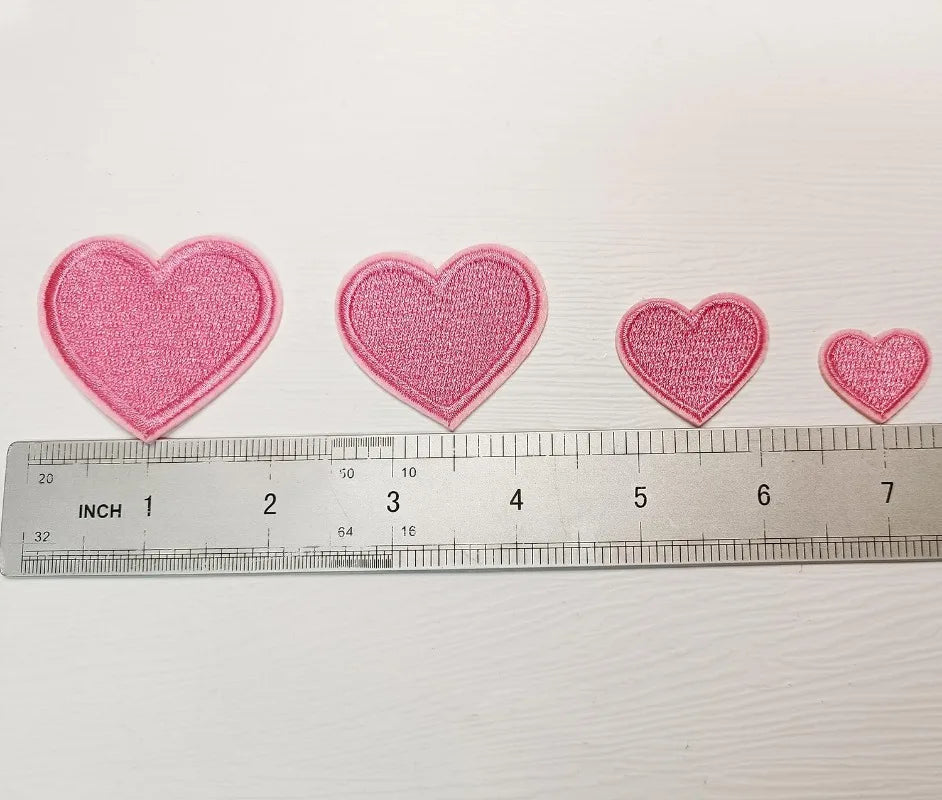 A row of pink iron-on love heart embroidered patches laid out next to a ruler.
