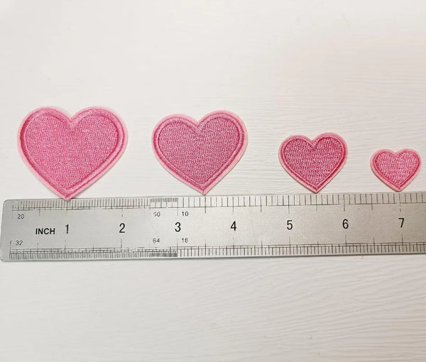 A row of pink iron-on love heart embroidered patches laid out next to a ruler.