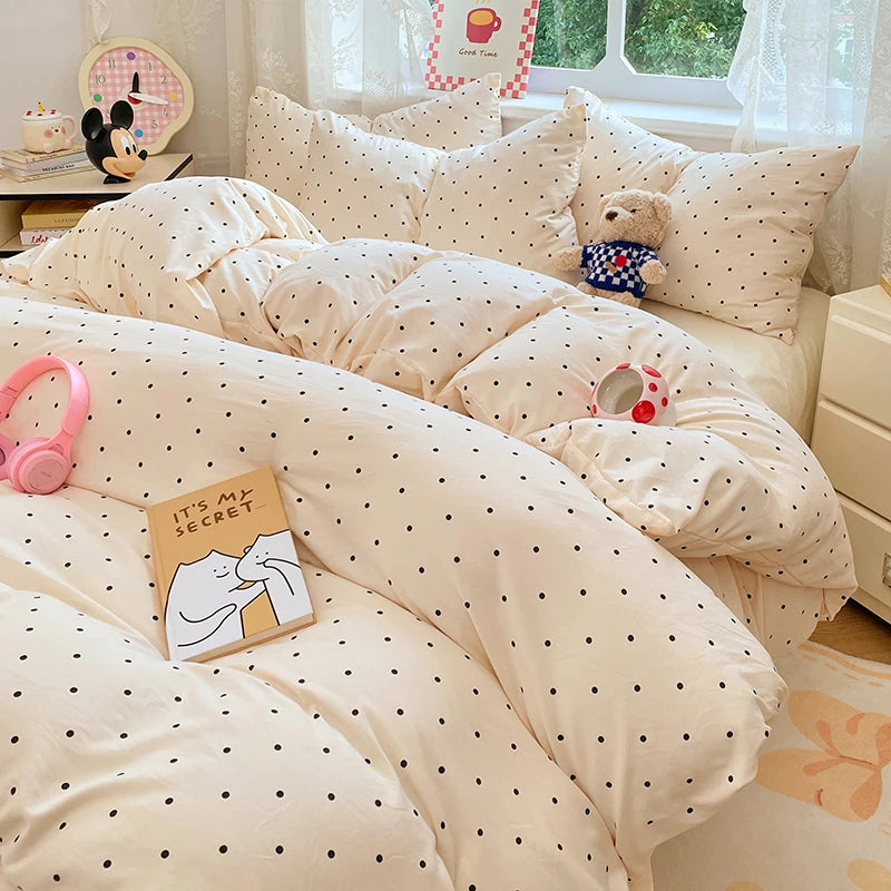 A beige polka-dot duvet cover set with matching pillowcases and a stuffed animal on a bed.
