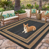 A black and gold reversible outdoor patio rug with a patterned design placed on a stone patio.