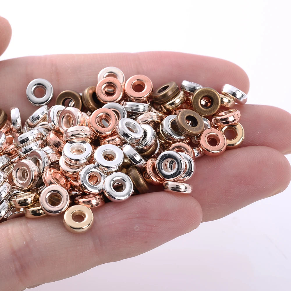 A hand holds a mix of colorful geometric acrylic beads in various gold and silver tones for jewelry making